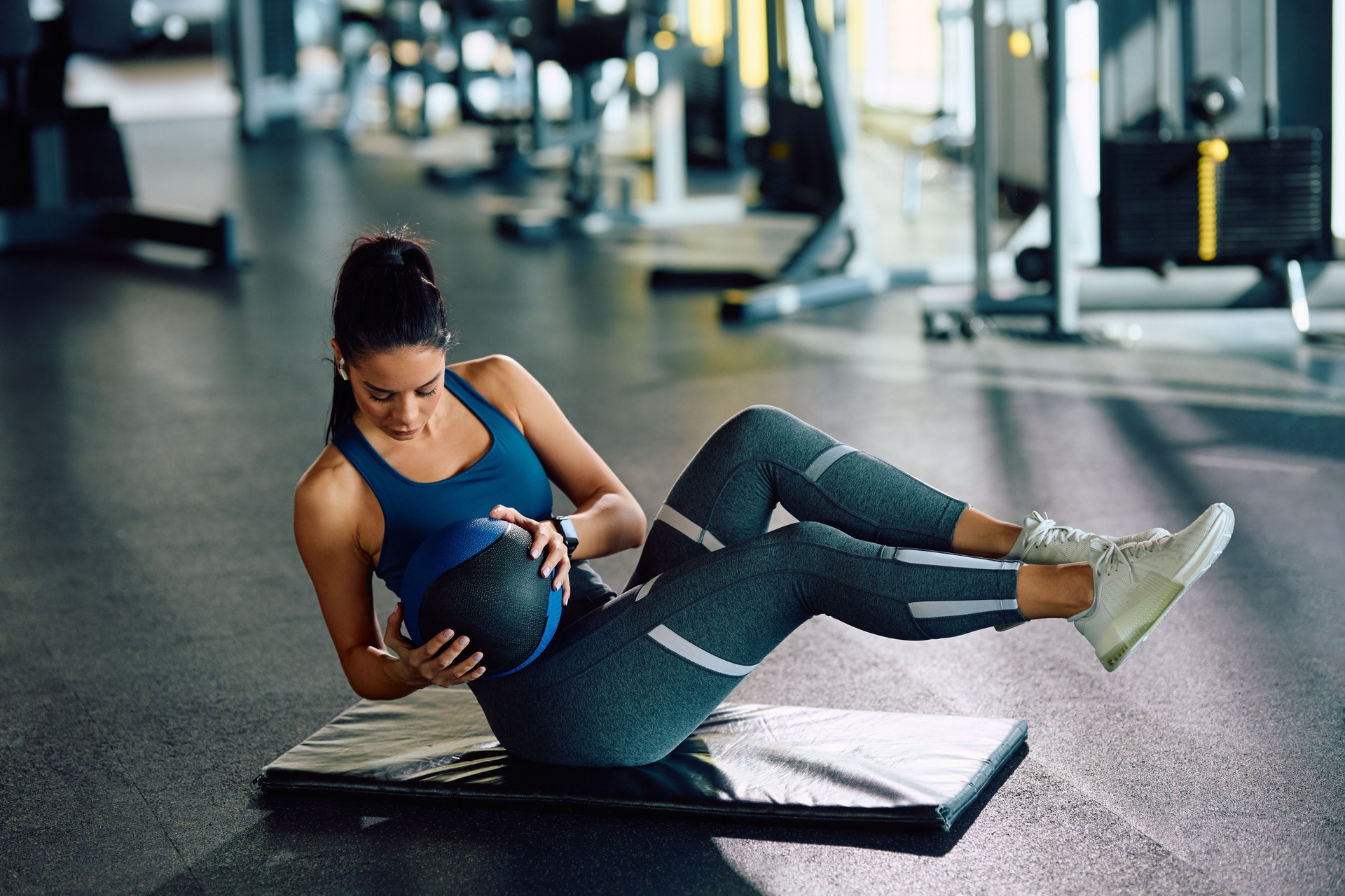 Young sportswoman doing side sit-ups with medicine ball while exercising in health club.